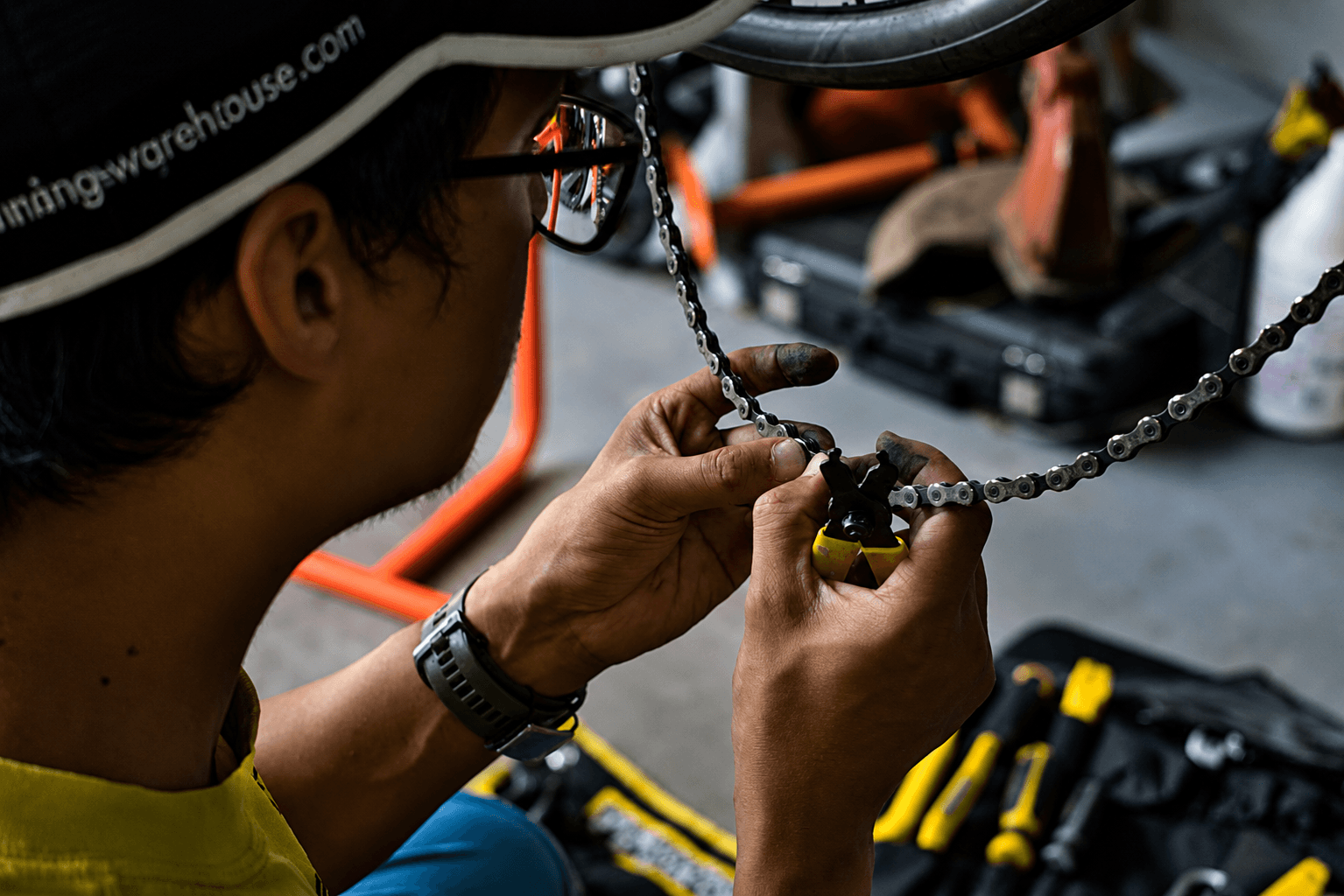 Close-up of a mechanic working on a bicycle chain inside a workshop, showcasing precision and manual skill.